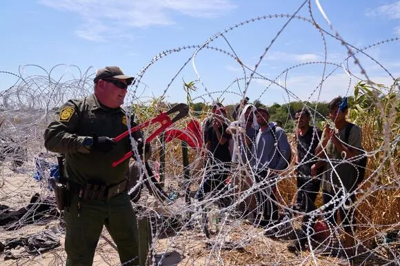 U.S. Customs and Border Protection officers cut concertina wire to let migrants who crossed the Rio Grande river from Mexico into the United States cross to be processed and transported.